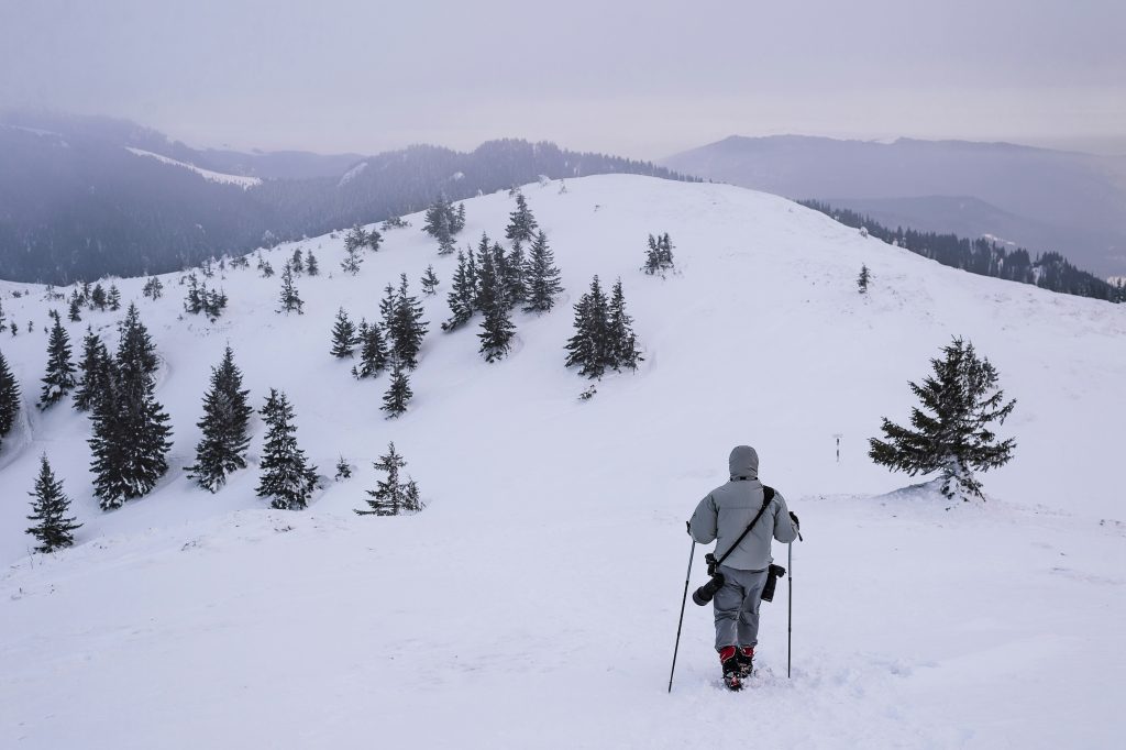 Proteger tu equipo fotográfico en invierno. Un fotógrafo caminando por la nieve con su equipo